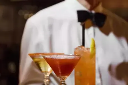 A server wearing a bowtie presents a tray of cocktails at Absinthe Restaurant in 贝博体彩app.